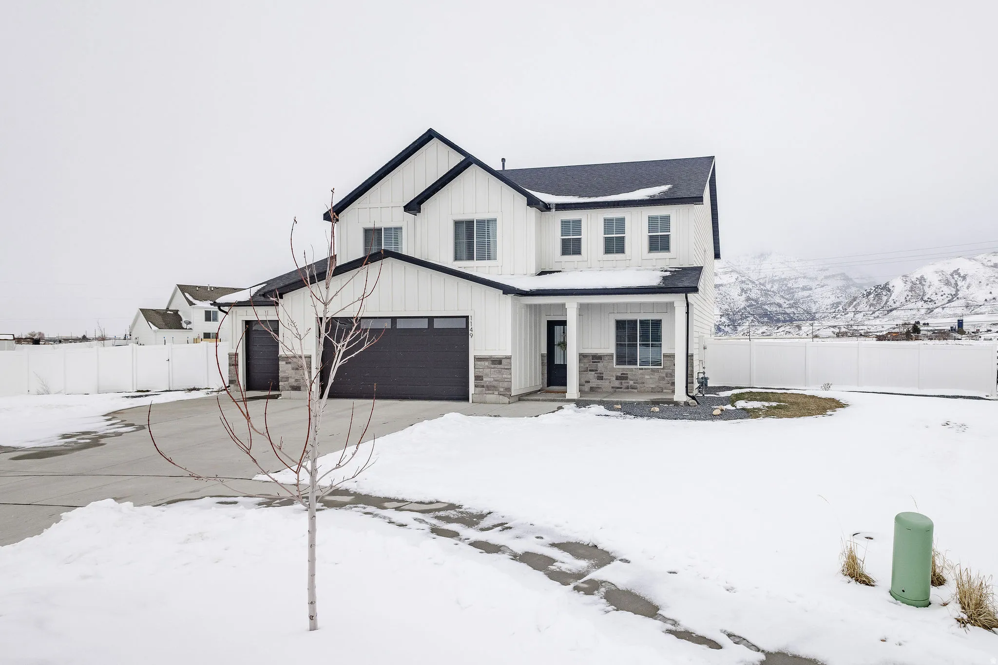 Modern farmhouse-style exterior featuring white vertical and horizontal siding, dark roof, dark garage doors, stone veneer accents, and a covered front porch with white pillars