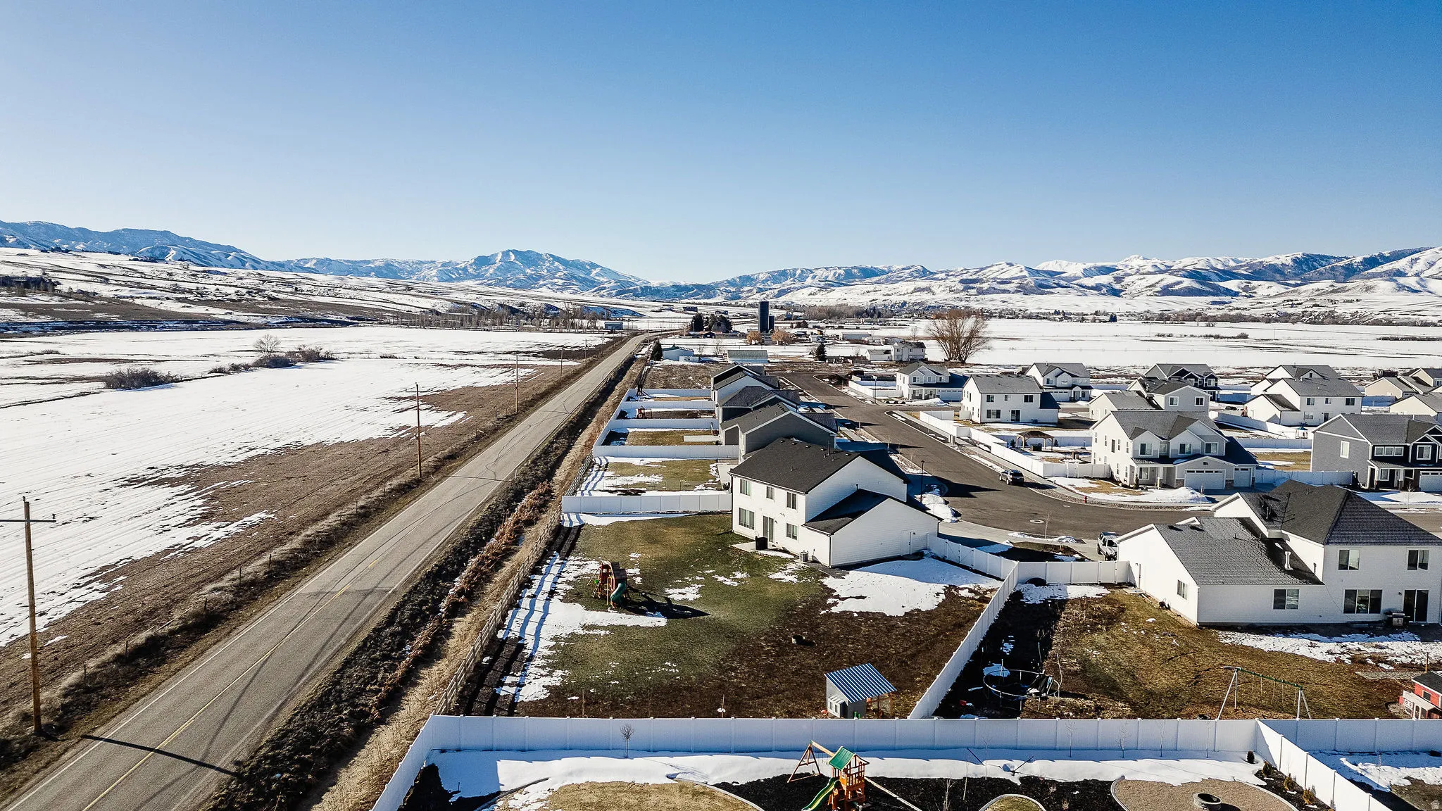 New construction homes with white exteriors and dark roofing, featuring paved streets and individual white privacy fences