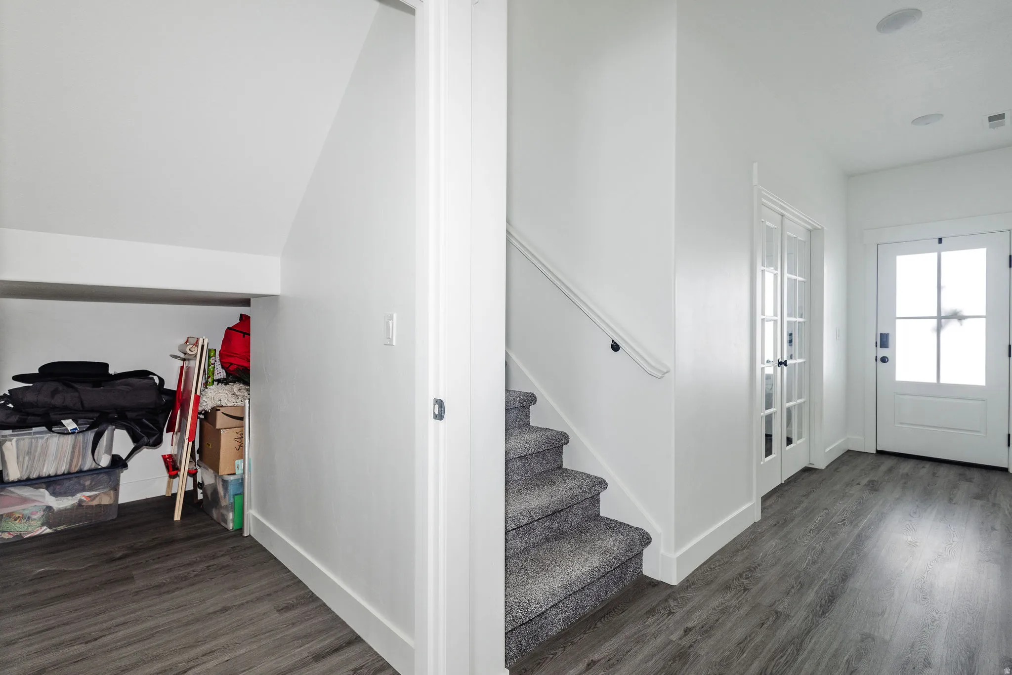 Foyer featuring wood-finish flooring, a carpeted staircase with white railing, and a white front door with glass lites