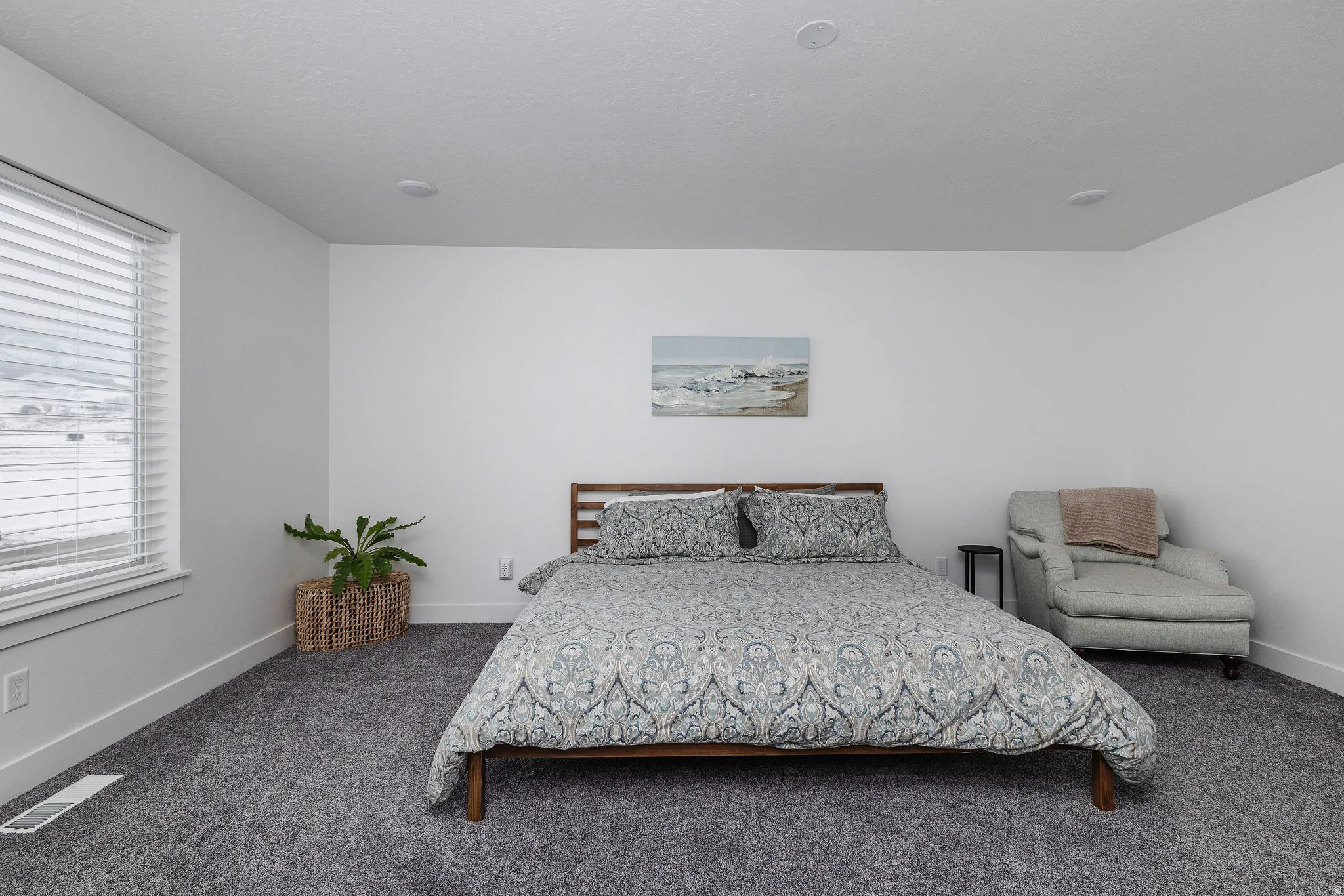 Spacious room featuring neutral white walls, dark gray carpet, a large window with white blinds, and recessed ceiling lighting