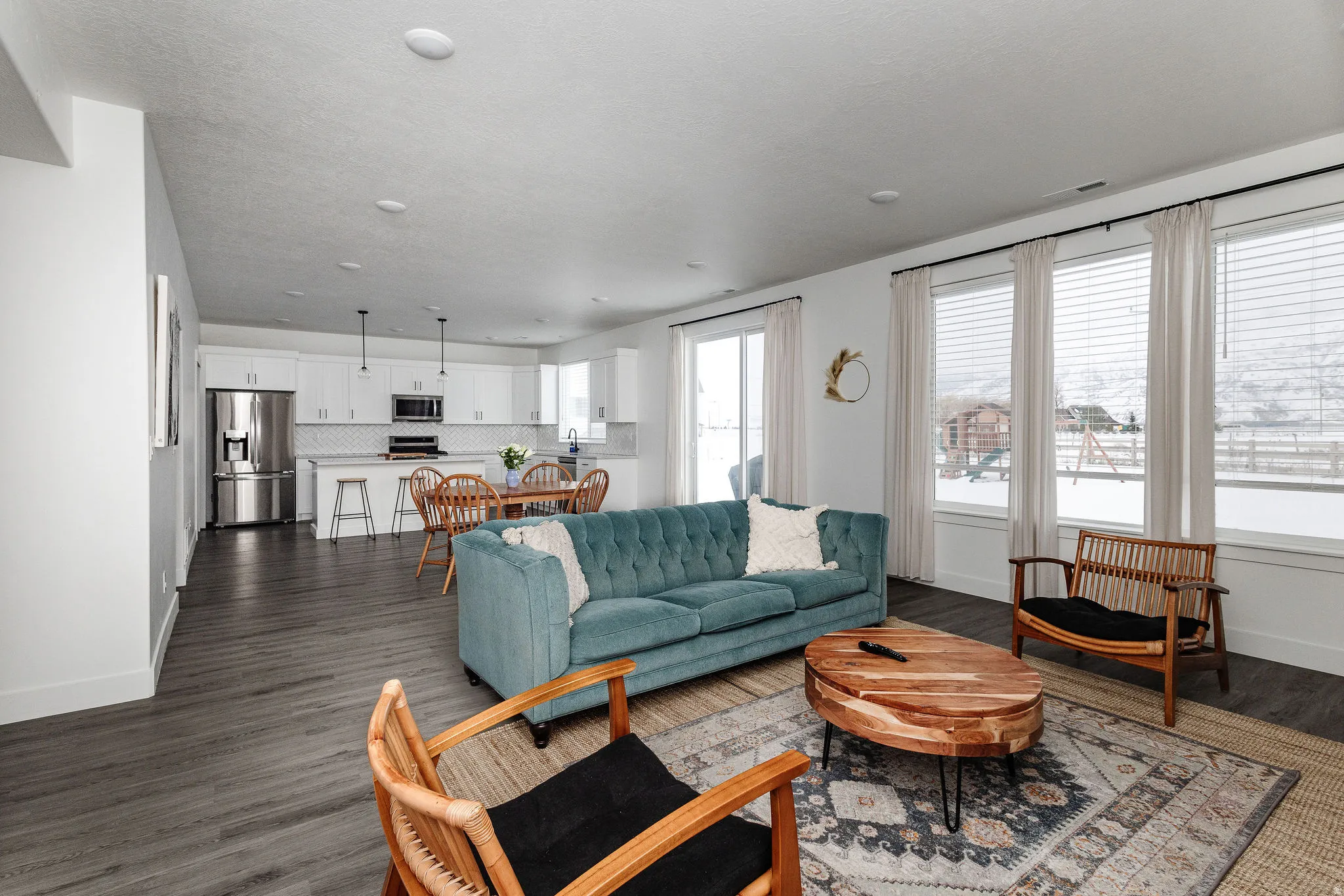Open-concept living area featuring wood-finish flooring, recessed lighting, and a kitchen with white cabinetry, stainless steel appliances, and a tiled backsplash