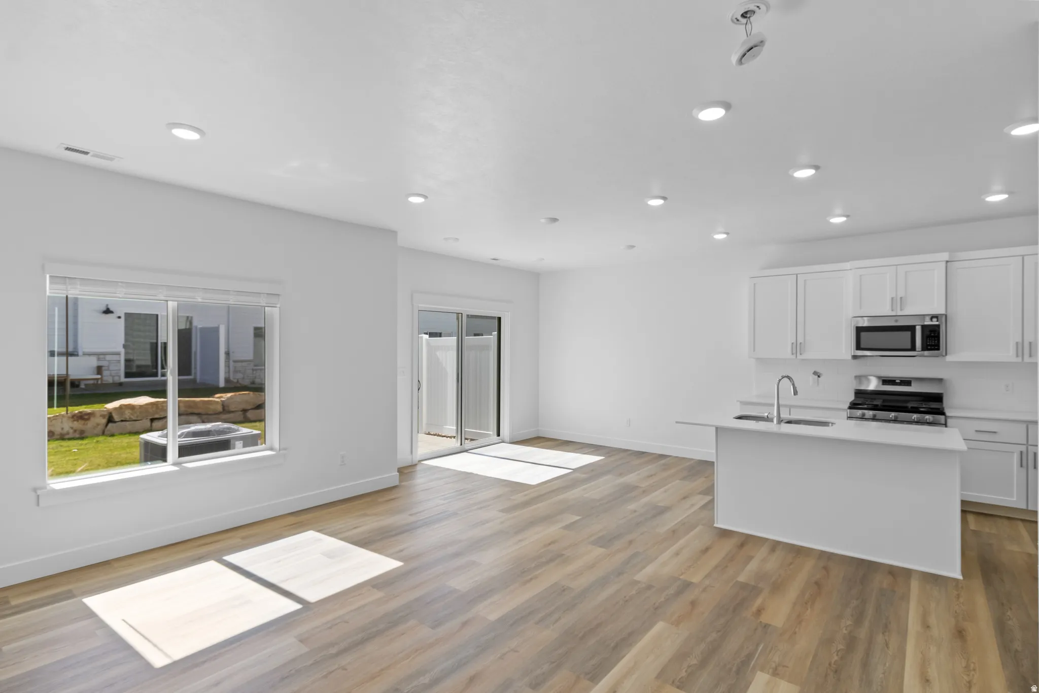 Open-concept living space featuring wood-finish flooring, recessed lighting, and a white kitchen with stainless steel appliances