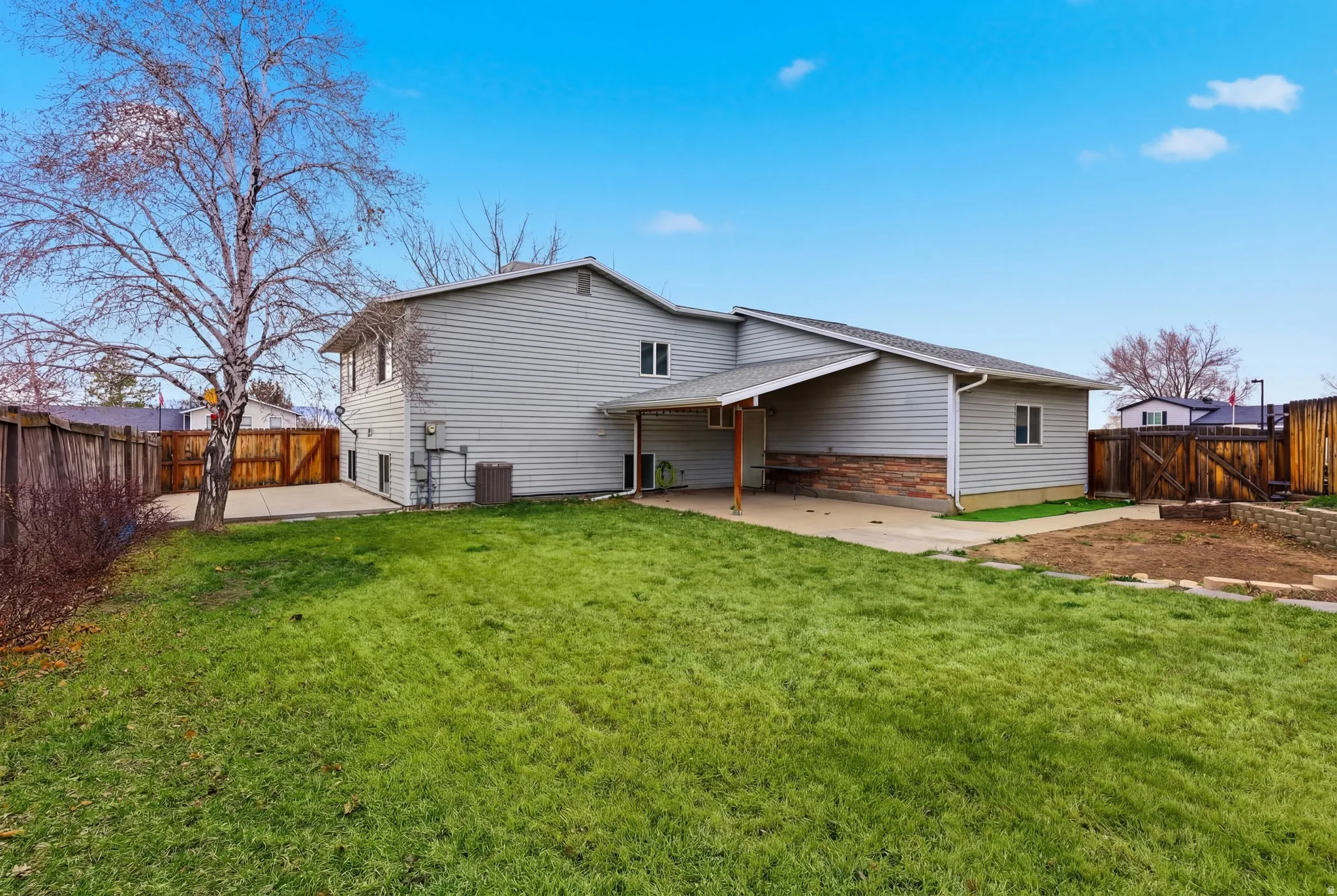 Expansive rear yard featuring green lawn, mature tree, and concrete patio spaces