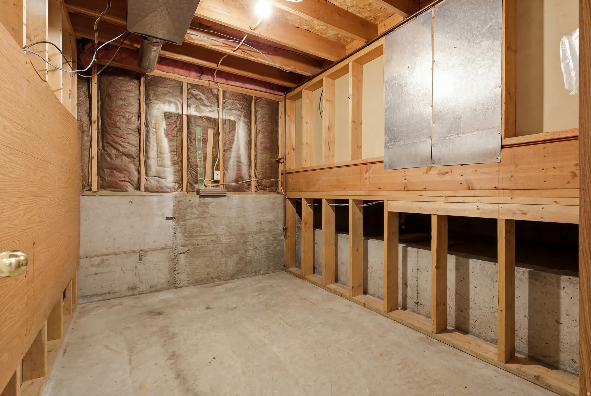 Unfinished storage space featuring exposed concrete foundation, framed walls, visible insulation, and overhead ductwork