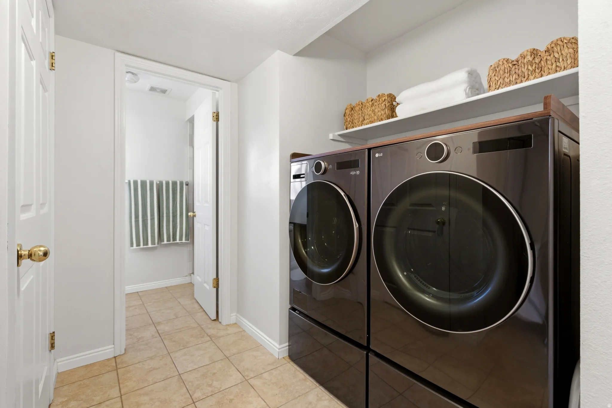 Dedicated laundry area featuring a front-loading washer and dryer set, an integrated shelf, and tile flooring