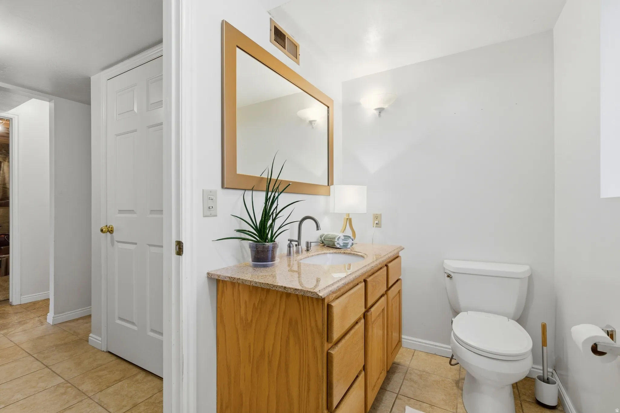 Bathroom featuring a wood-finish vanity with a light-toned countertop, a rectangular mirror, and sconce lighting