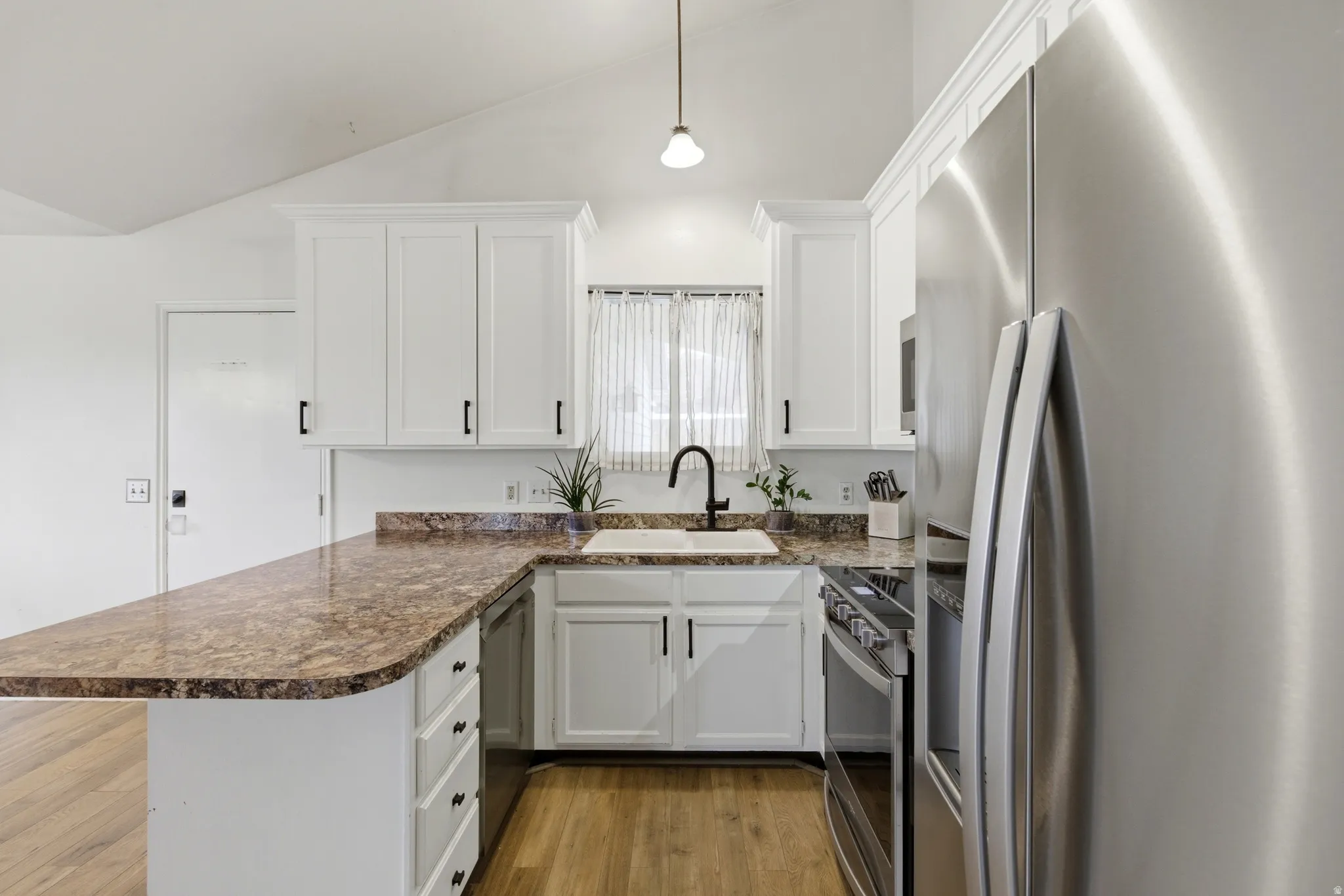 Kitchen featuring white shaker cabinetry, stainless steel appliances, wood-finish flooring, a speckled countertop, and a white farmhouse sink with a matte black faucet