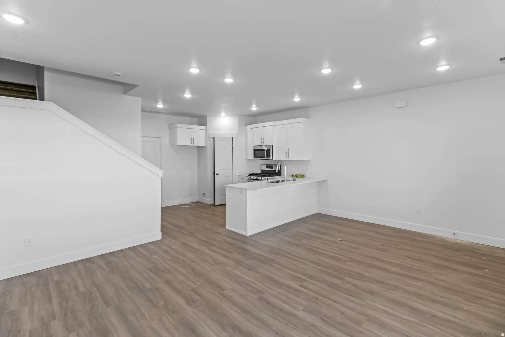 Open-concept living area featuring wood-finish flooring, recessed lighting, and a kitchen with white cabinetry and stainless steel appliances