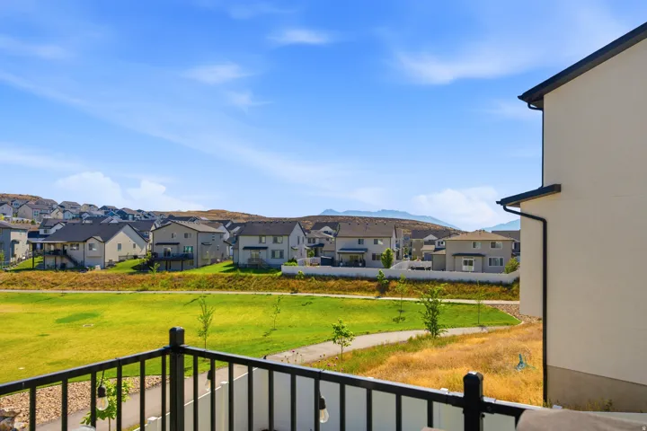 Balcony overlooking a green expanse with a paved pathway, bordered by residential properties and distant hills