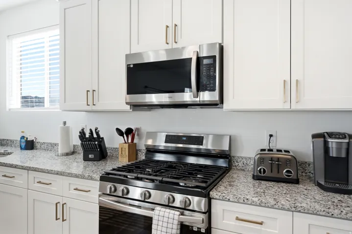 Kitchen featuring white shaker cabinetry with gold-toned hardware, speckled countertops, a stainless steel gas range, and an over-the-range microwave