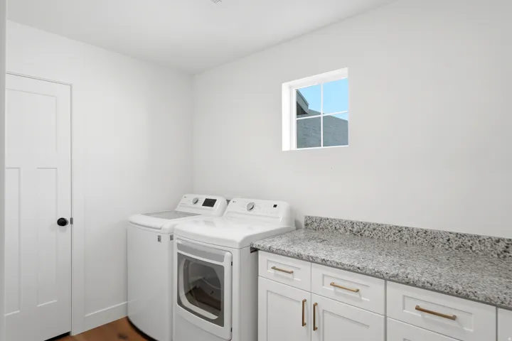 Laundry area featuring a window, white cabinetry with bronze hardware, a light-toned speckled countertop, and wood-finish flooring