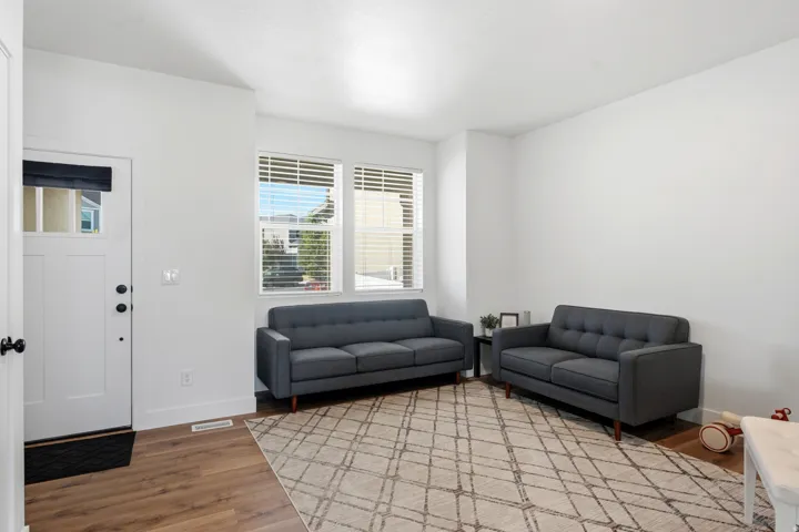 Bright living area featuring wood-finish flooring, white walls, and multiple windows with horizontal blinds