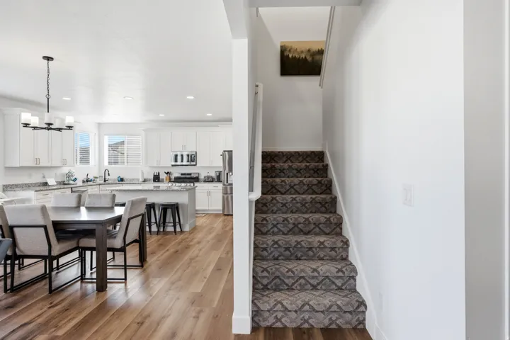 Open-concept living space featuring wood-finish flooring throughout, a modern kitchen with white cabinetry, stainless steel appliances, and a central island with bar seating