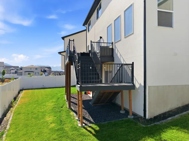 Exterior featuring a multi-level deck with black railings, a full privacy fence, and a manicured lawn
