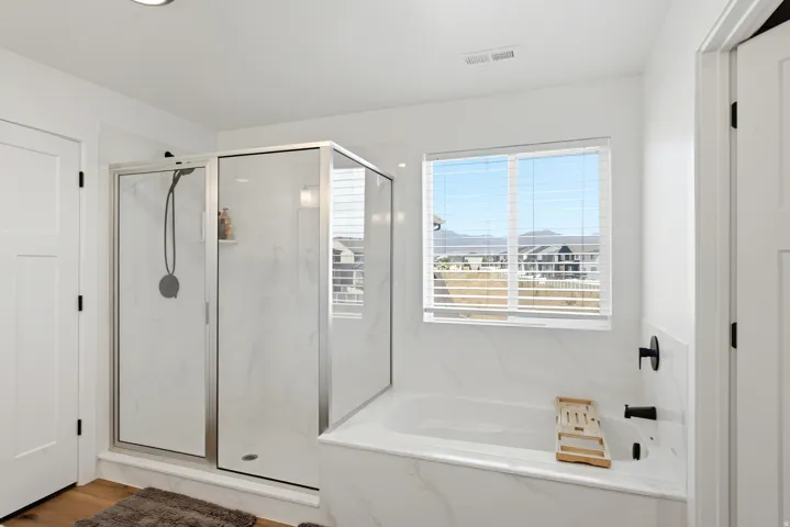 White tiled bathroom featuring a walk-in shower with a glass enclosure and a separate soaking tub with black fixtures