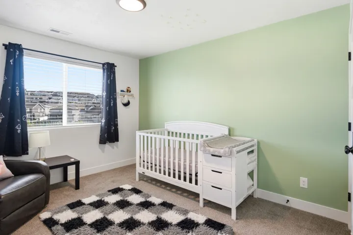 Spacious room featuring a large window, light green accent wall, neutral carpeting, white baseboards, and a ceiling-mounted light fixture