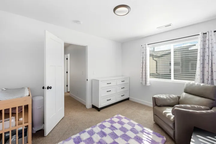 Bright room featuring a window with horizontal blinds and decorative curtains, white walls, and neutral carpet flooring