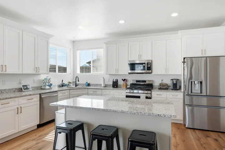 Modern kitchen featuring white shaker cabinetry, stainless steel appliances, speckled stone countertops, and wood-finish flooring