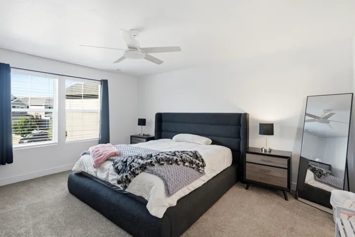 Bedroom featuring a ceiling fan, two windows with blinds, and neutral-toned carpeting