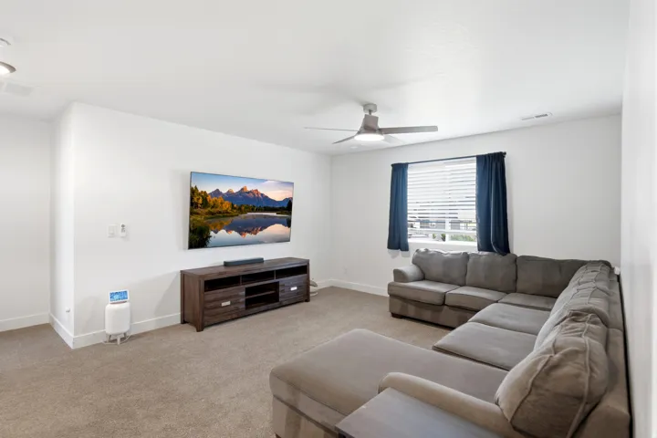 Spacious room featuring carpeted flooring, a ceiling fan with integrated lighting, and a window with horizontal blinds and drapery