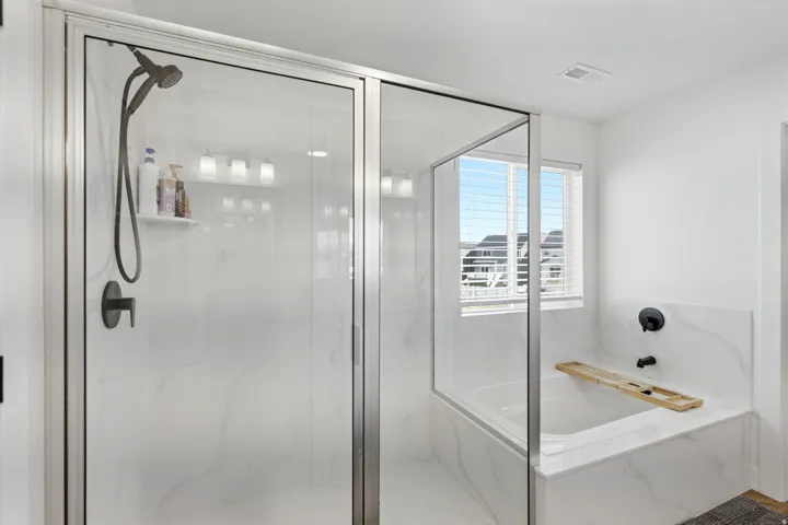 Contemporary bathroom featuring a glass-enclosed shower with matte black fixtures, a built-in tub with matching surround, and a window with blinds
