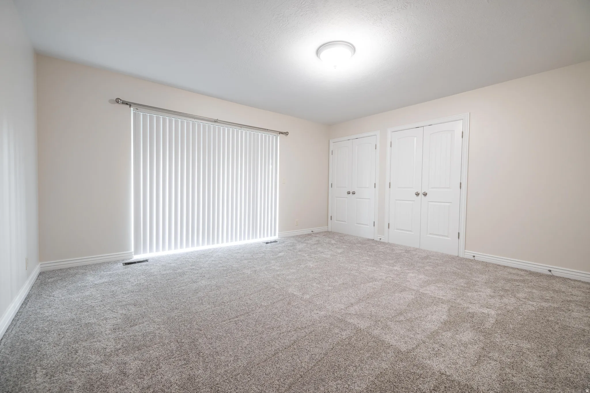 Spacious room featuring neutral-toned walls, new carpet flooring, and a large sliding glass door leading to balcony.