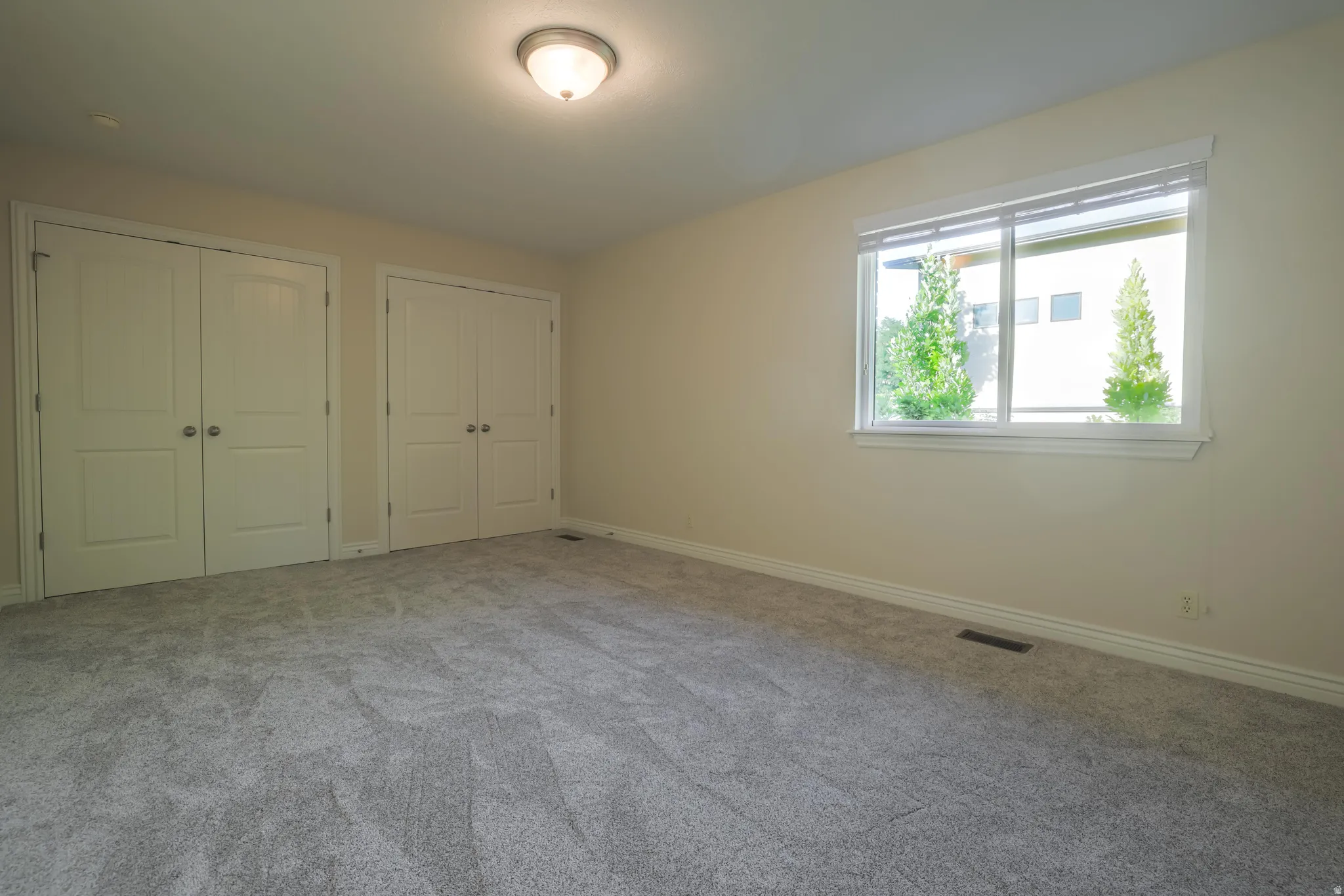 Spacious room featuring light-colored walls, gray carpet flooring, and white trim