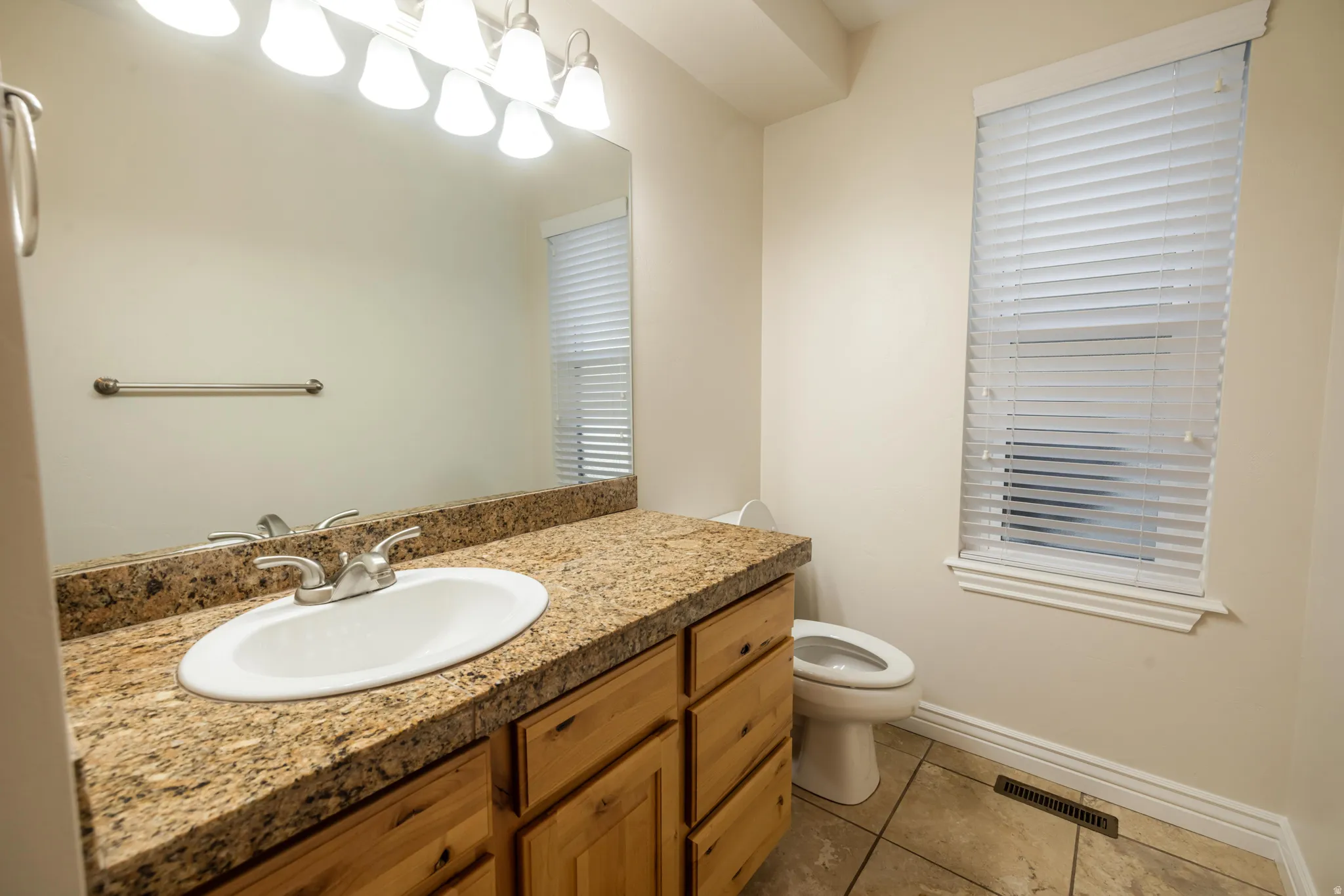 Bathroom featuring a single vanity with an oval undermount sink, a stone countertop, and wood-finish cabinetry