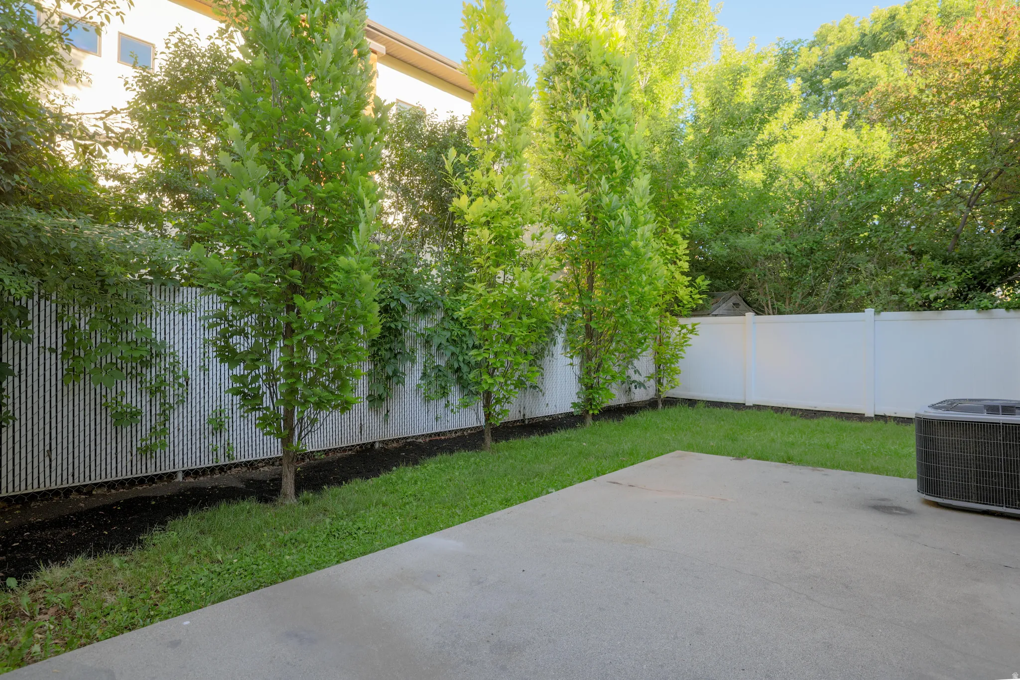 Private backyard featuring a concrete patio, manicured lawn, and mature trees