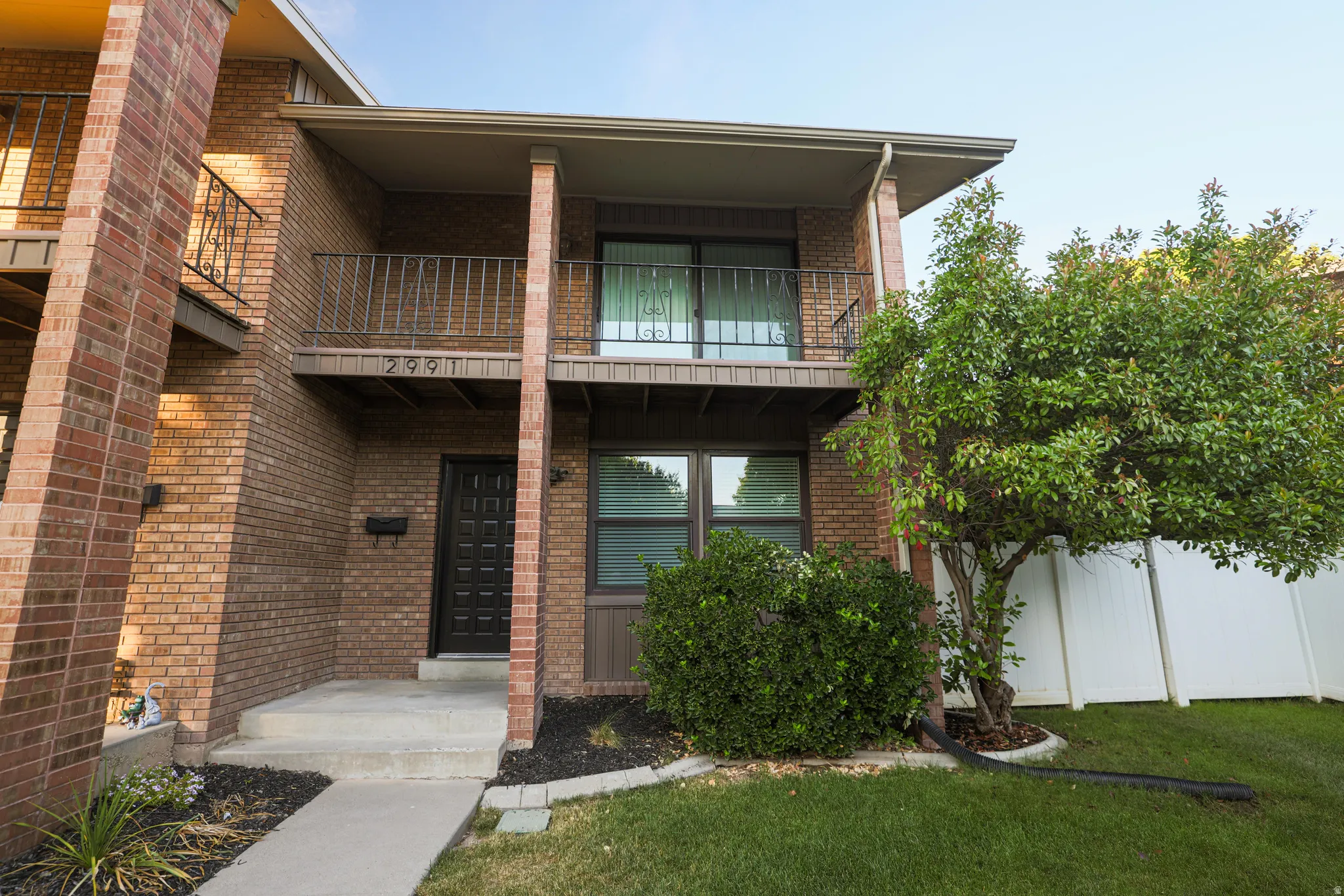 Brick exterior featuring a private balcony with wrought iron railing, concrete entry porch, and ground-level windows