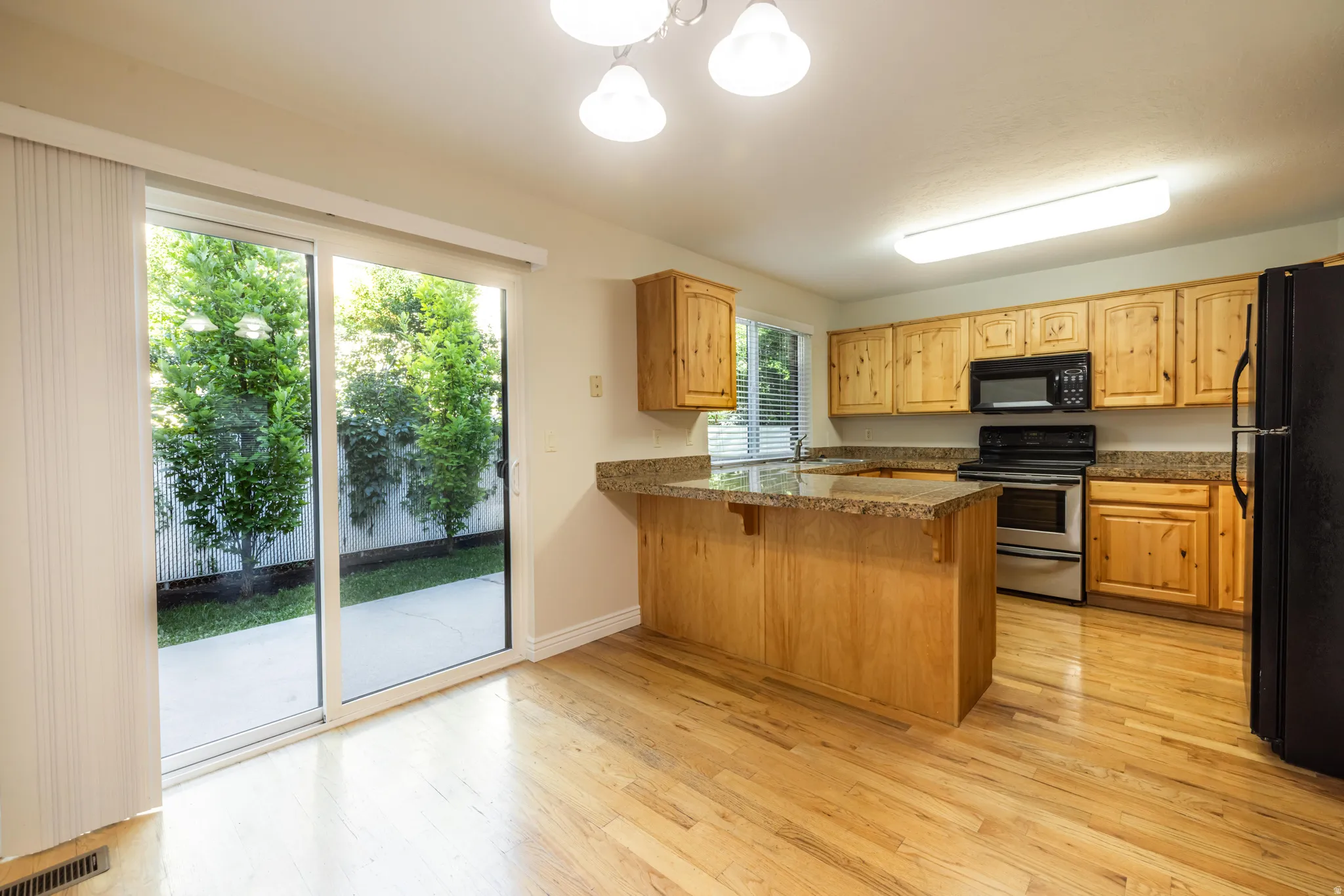 Kitchen featuring wood cabinetry, stone-finish countertops, stainless steel appliances, and wood-finish flooring