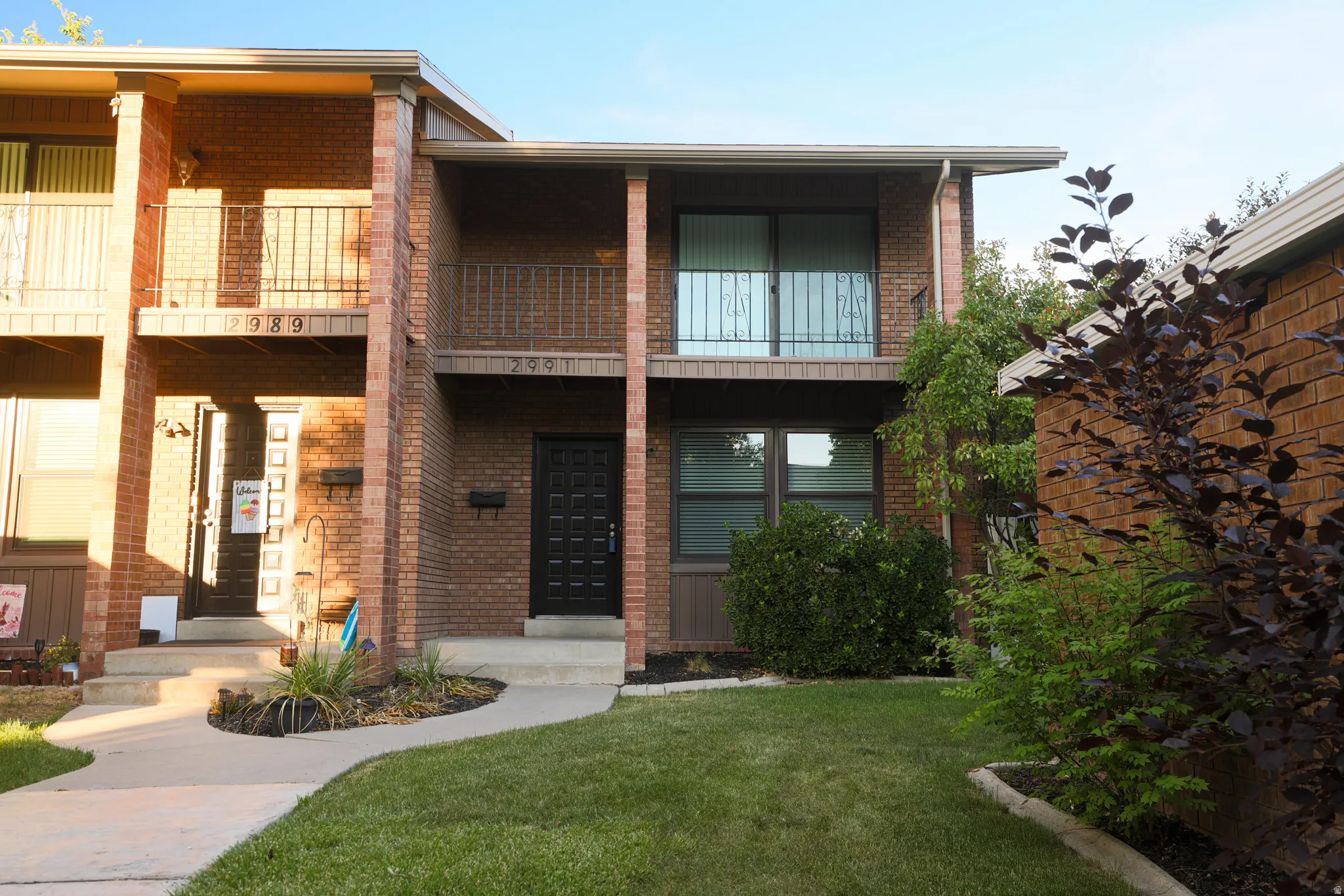 Brick exterior featuring a black front door, a second-story balcony with metal railings, and a well-maintained lawn