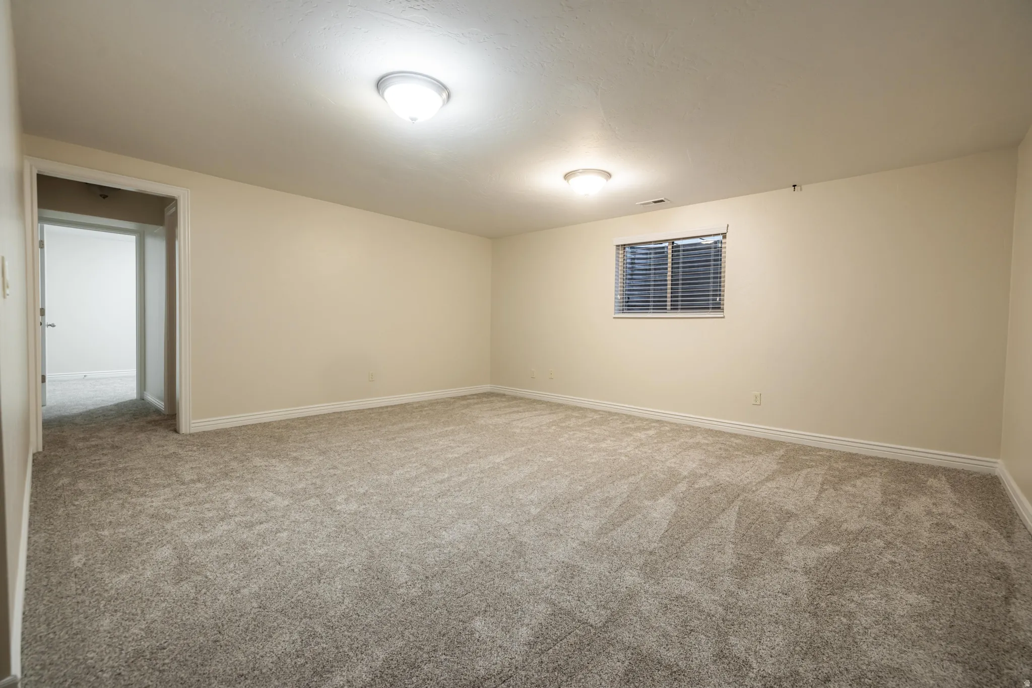 Spacious room featuring neutral carpeting, light-toned walls, and a window with horizontal blinds
