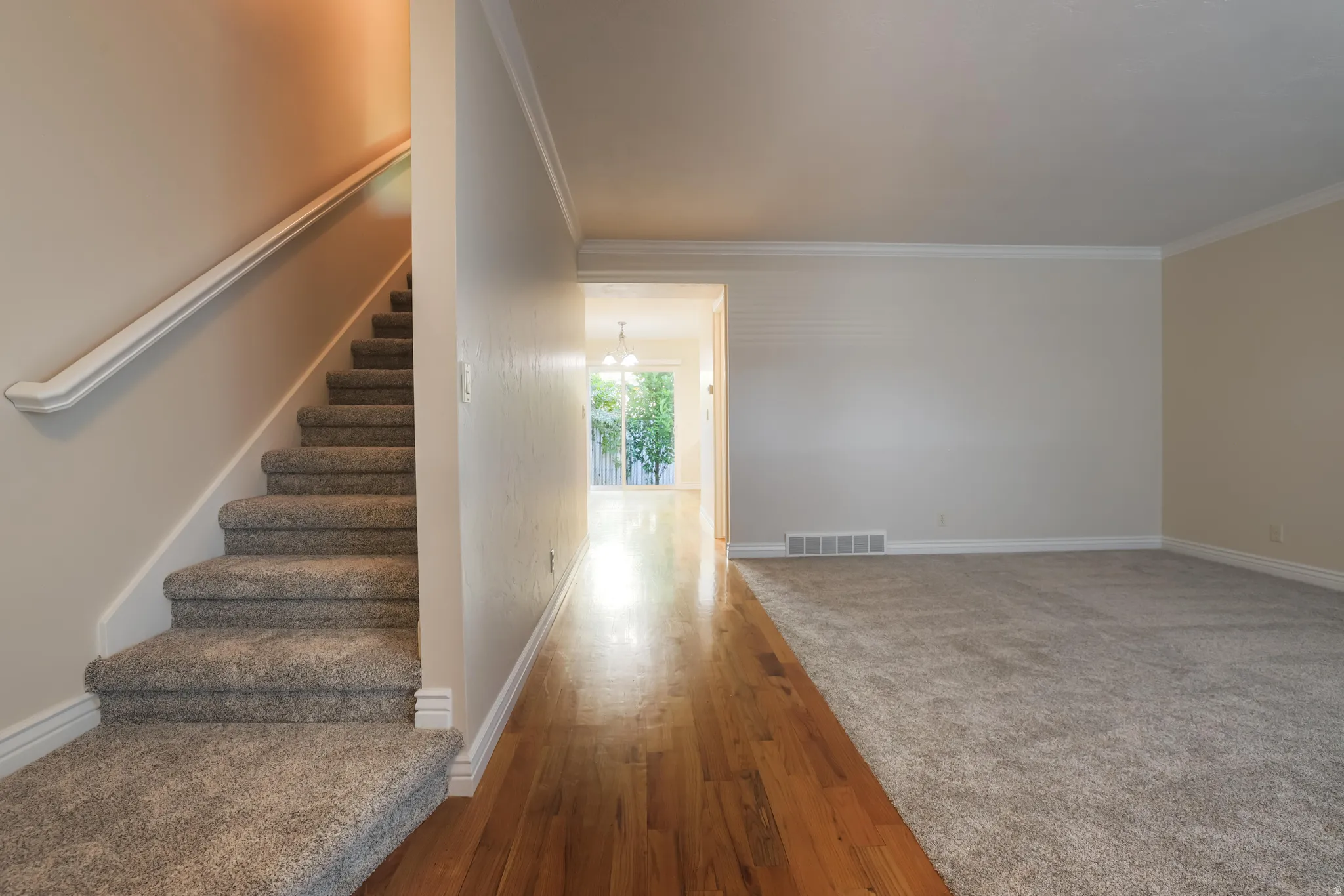 Entryway featuring a carpeted staircase with handrail, wood-finish flooring, and crown molding