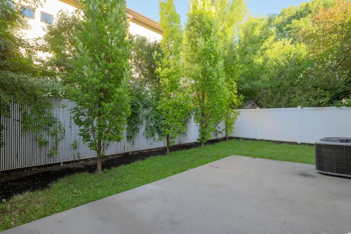 Private backyard featuring a concrete patio, manicured lawn, and mature trees
