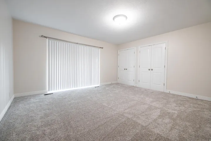 Spacious room featuring neutral-toned walls, new carpet flooring, and a large sliding glass door leading to balcony.