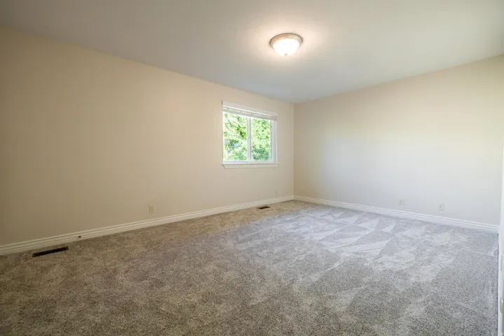 featuring textured carpet flooring, light-toned wall paint, a single window, white baseboards, and a ceiling-mounted light fixture