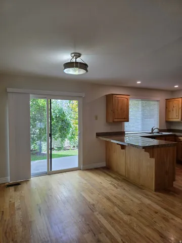 Wood-finish flooring, sliding glass door, recessed lighting, wood cabinetry, and granite-style countertops