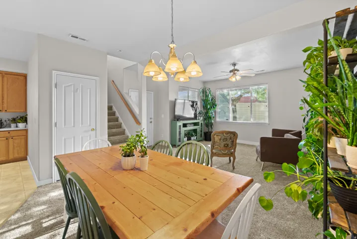 Open-concept living space featuring a dining area with a wood-finish table, an overhead chandelier, and a carpeted living room with a ceiling fan