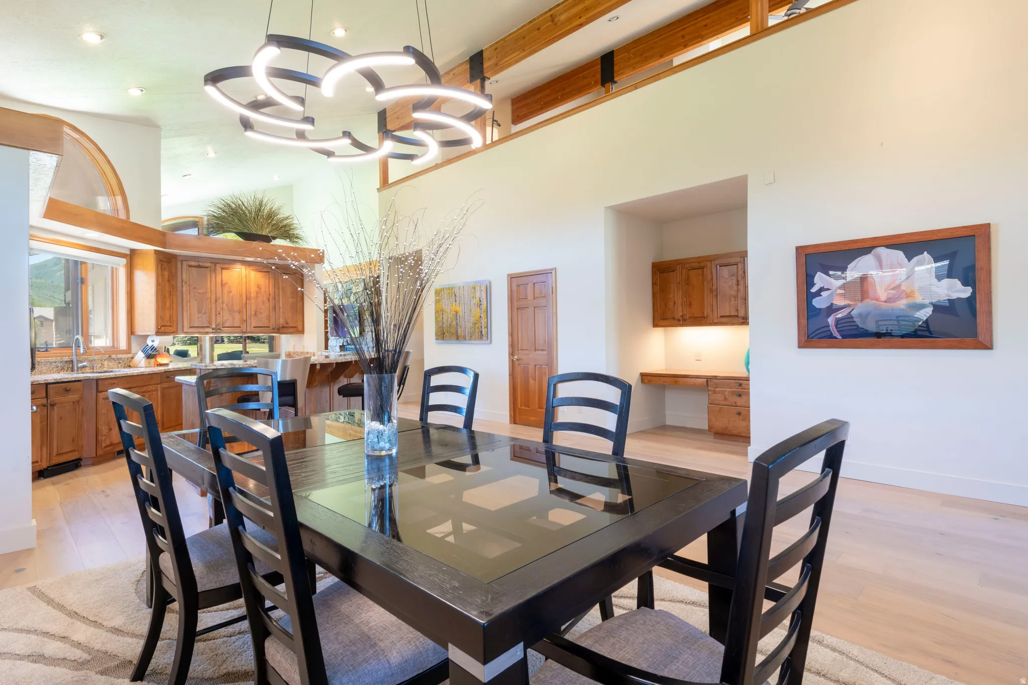 Dining area featuring a modern chandelier, wood-finish flooring, and a kitchen with wood cabinetry and stone countertops