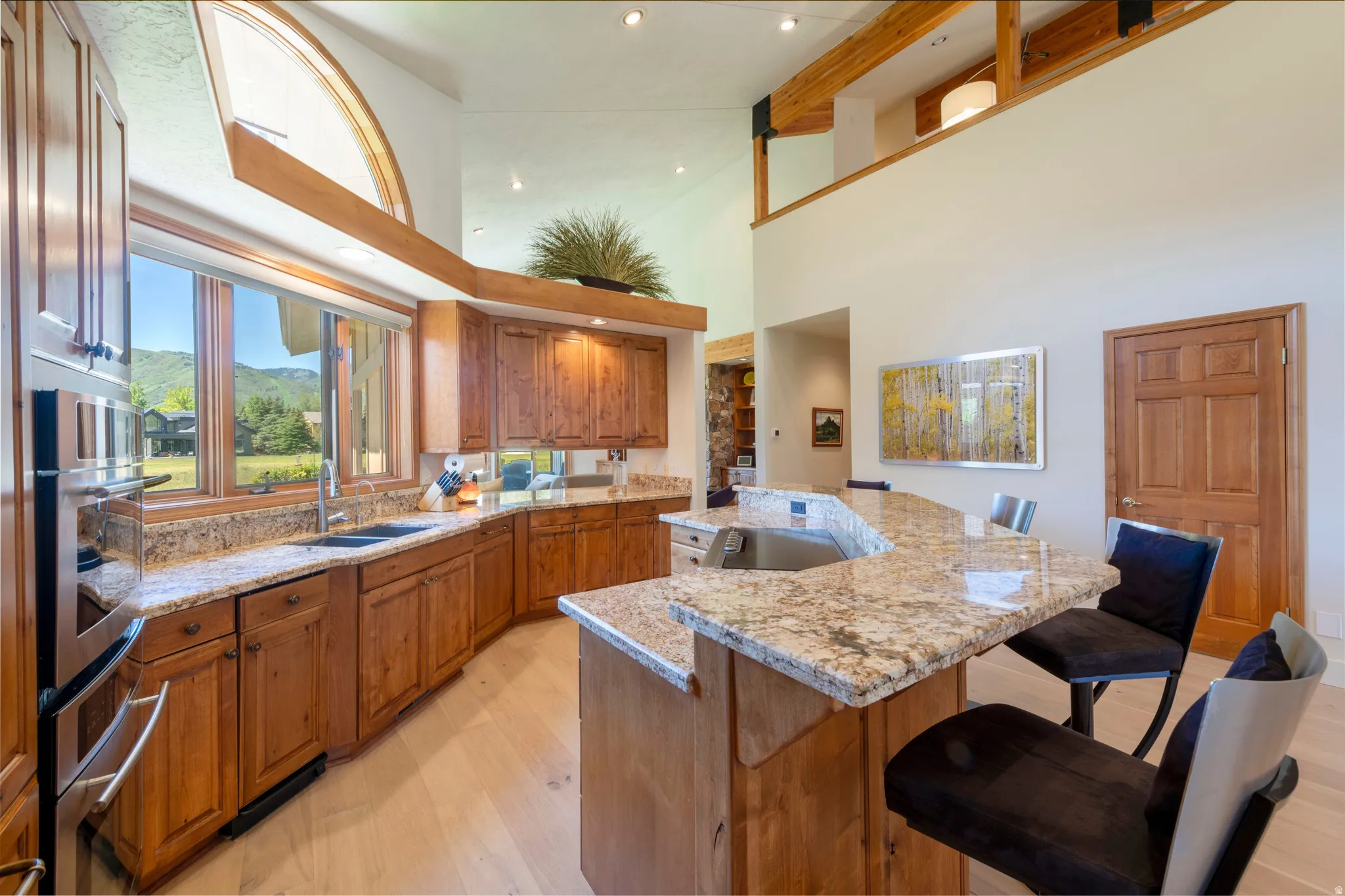 Spacious kitchen featuring light wood-finish flooring, abundant wood cabinetry, integrated stainless steel appliances, and a large granite-topped island with seating