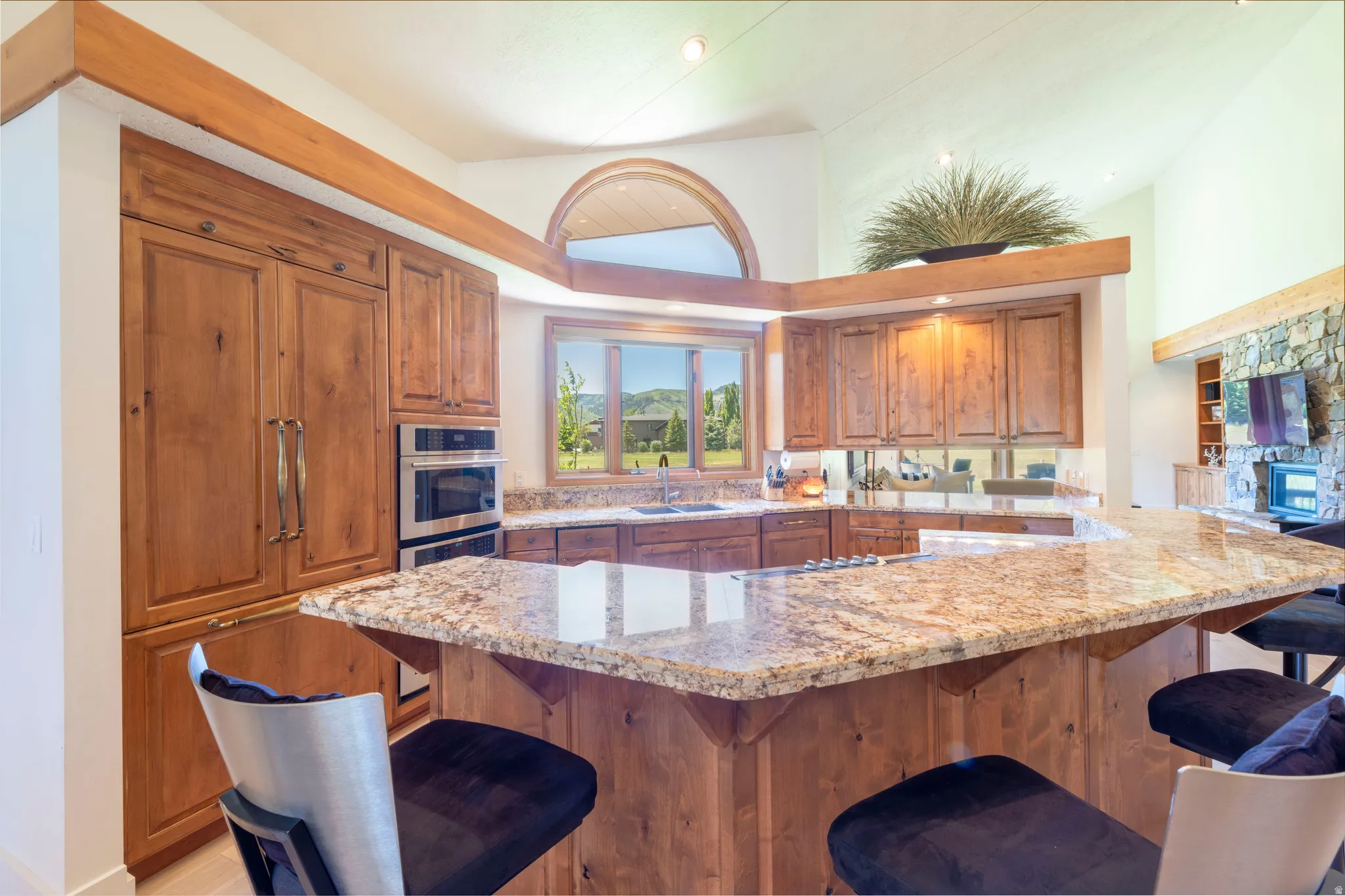 Spacious kitchen featuring an extended granite-finish island, integrated wood-paneled refrigerator, double wall ovens, wood cabinetry, and a mirrored backsplash