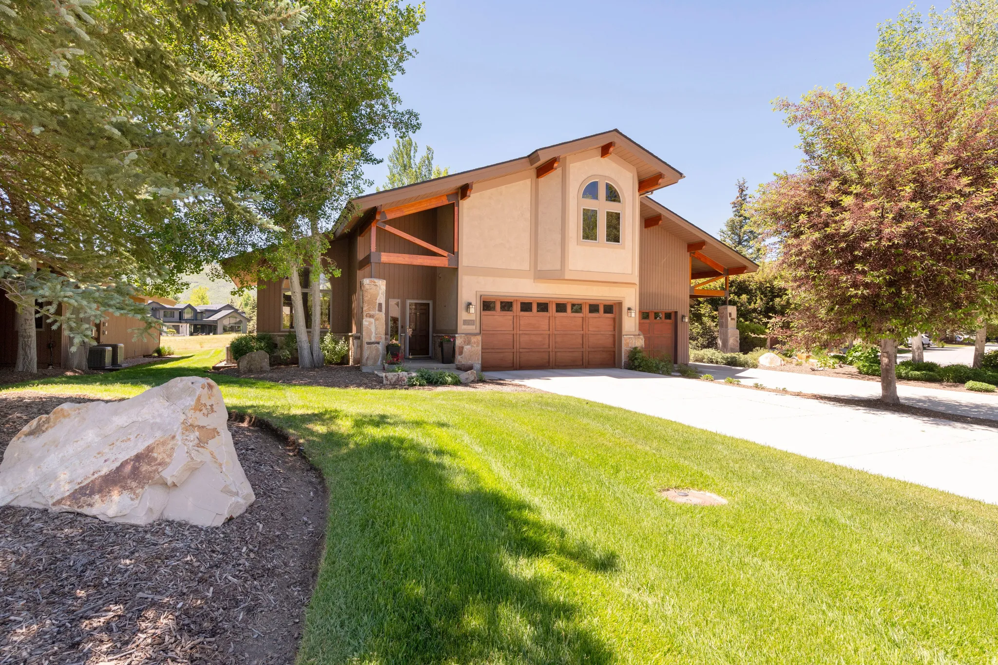 Two-story stucco home featuring a two-car garage with wood-finish doors, stone accent columns, exposed wood beams, and an arched window dormer