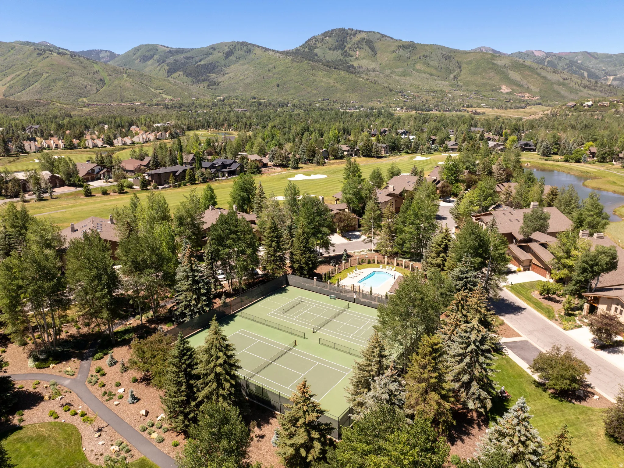 Outdoor recreation area featuring two tennis courts, an outdoor swimming pool, and surrounding mature trees