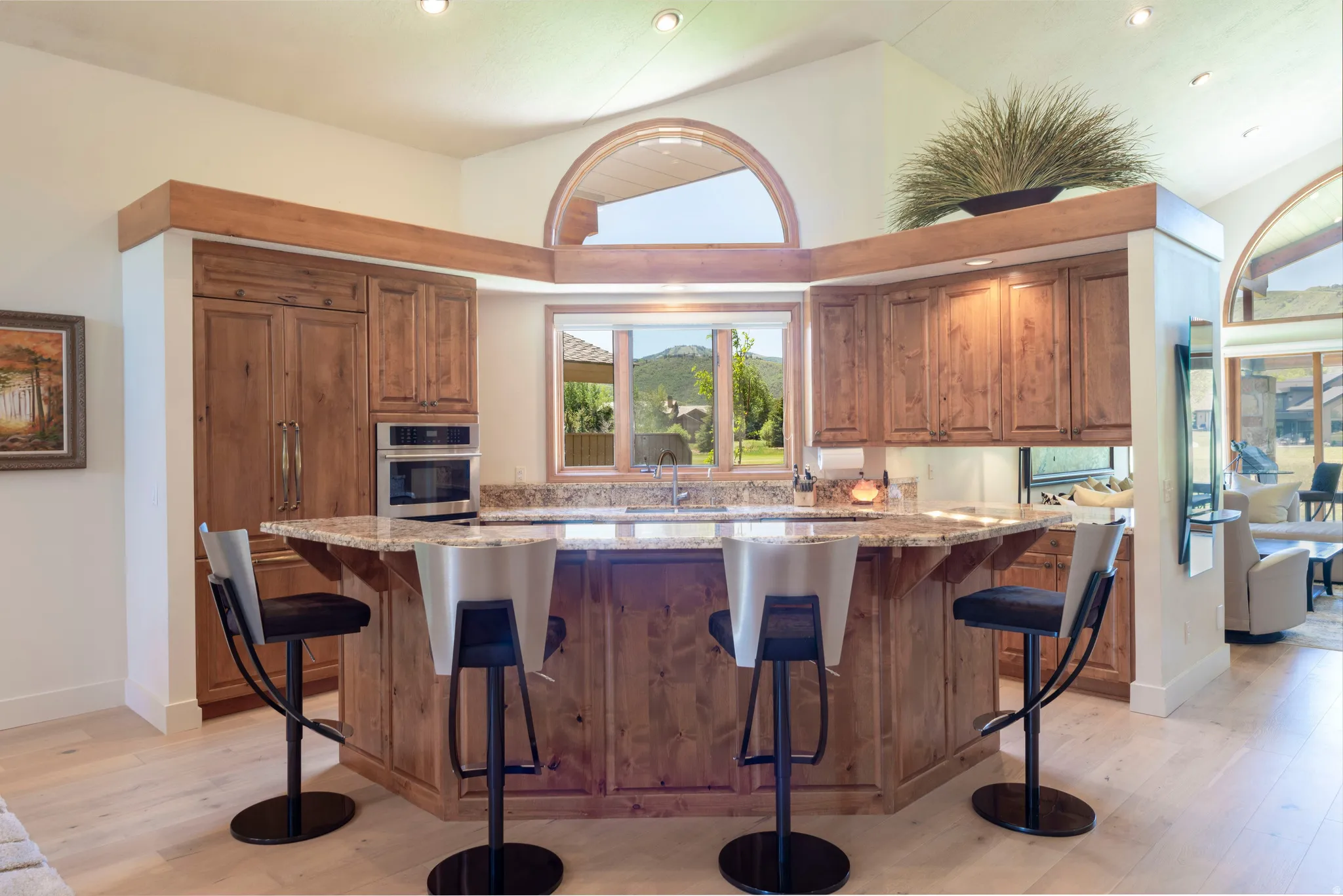 Spacious kitchen featuring light wood-finish flooring, a large island with a stone countertop, built-in stainless steel appliances, and abundant wood cabinetry