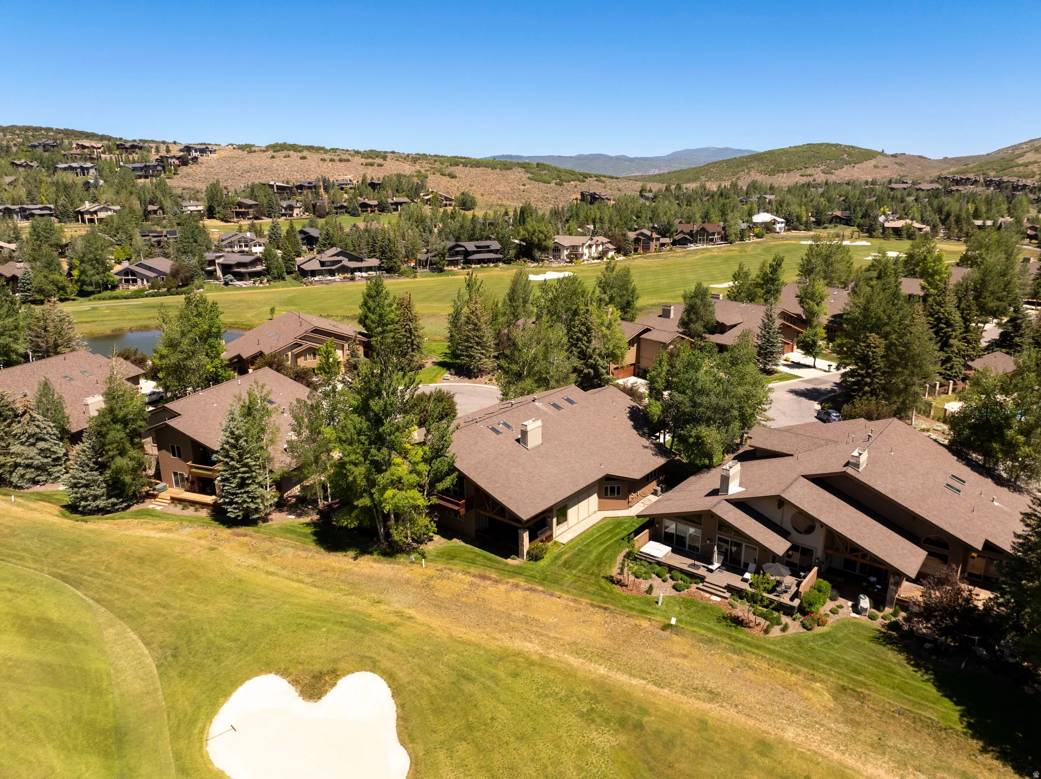 Expansive golf course community featuring multiple properties with pitched roofs, mature trees, and a pond