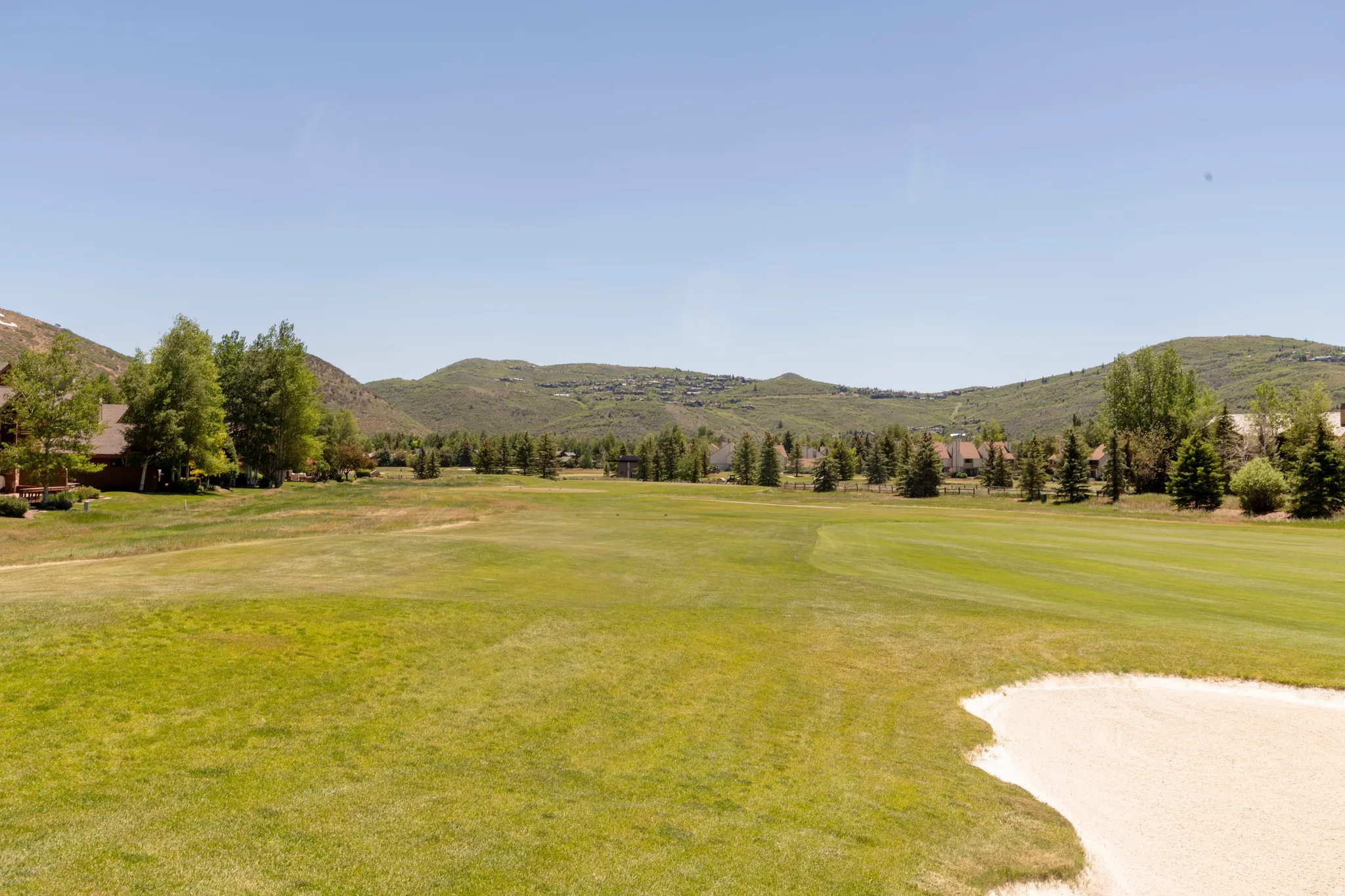 Expansive golf course green with a sand trap and distant mountain backdrop