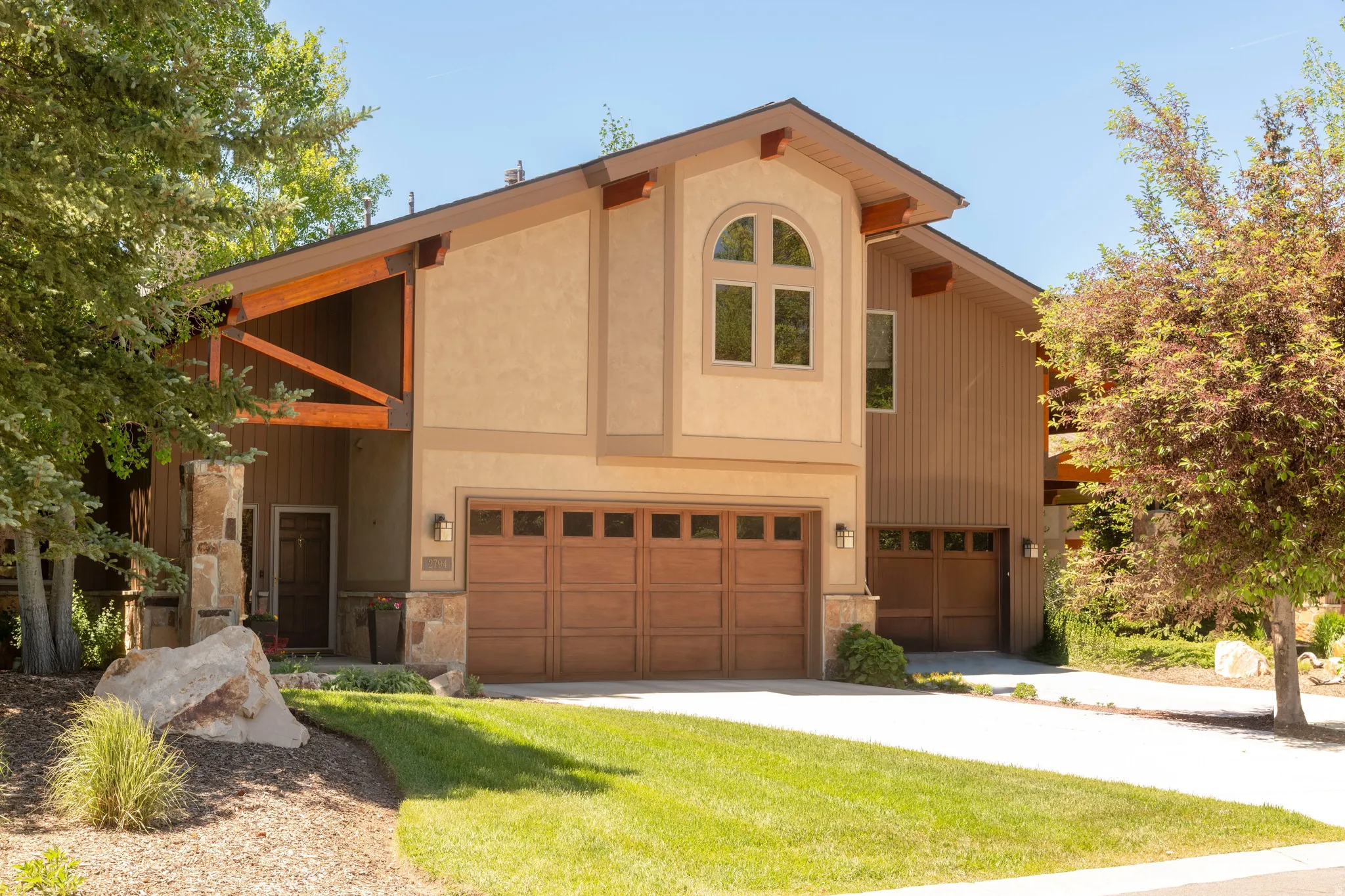Contemporary residence featuring a stucco and vertical siding exterior, arched window, exposed wooden beams, and two integrated garage doors