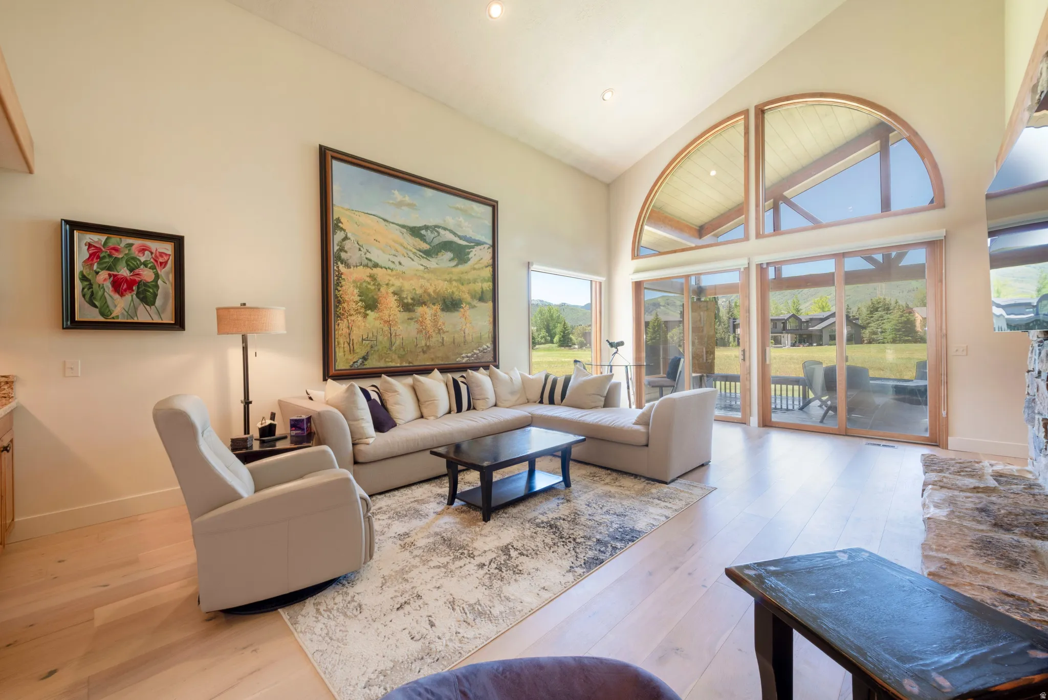 Living area featuring vaulted ceilings, light wood-finish flooring, and a stone fireplace