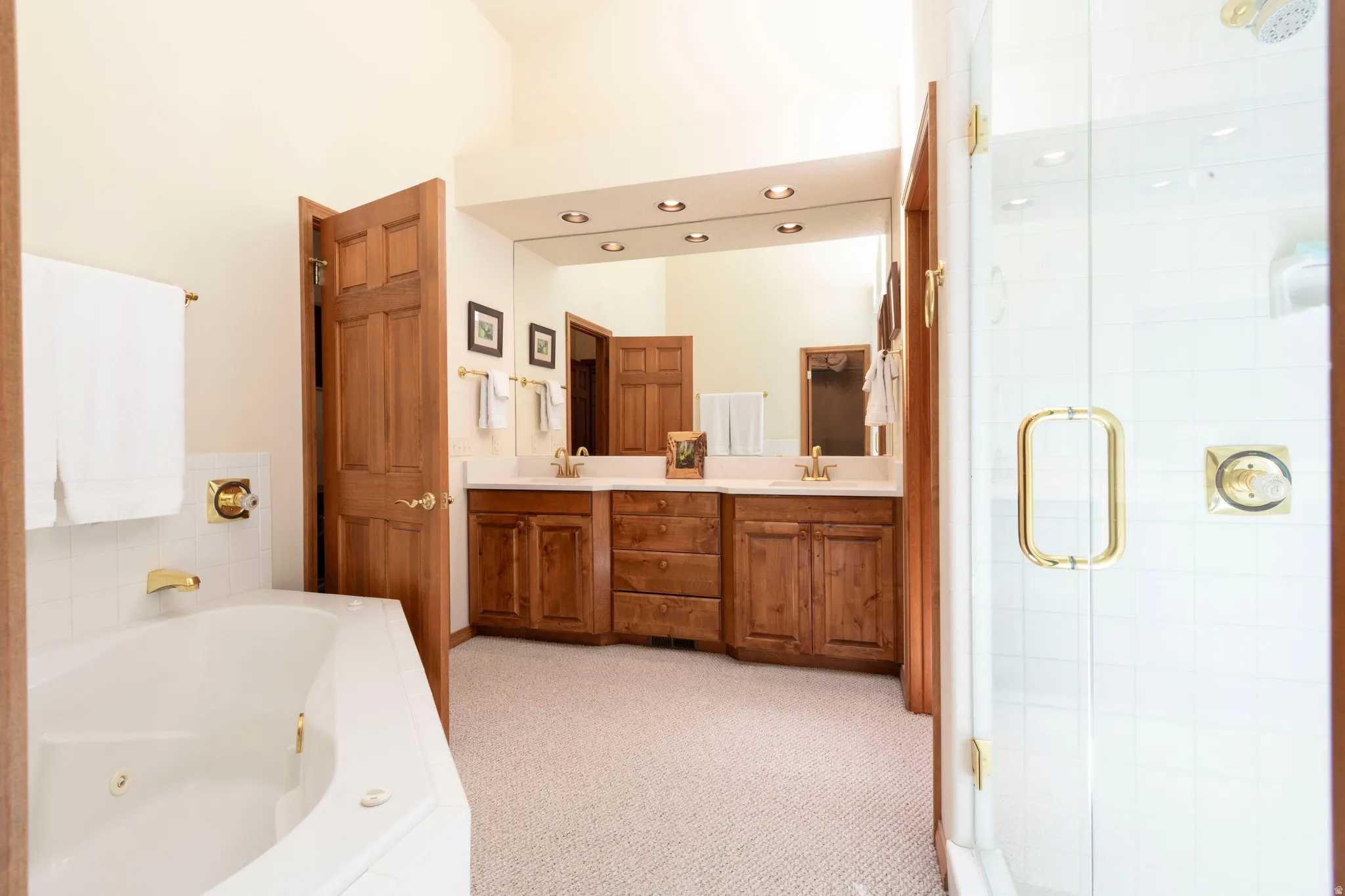 Spacious bathroom featuring a built-in jetted tub, a glass-enclosed shower, a dual-sink vanity with wood cabinetry, a large wall-mounted mirror, and recessed lighting